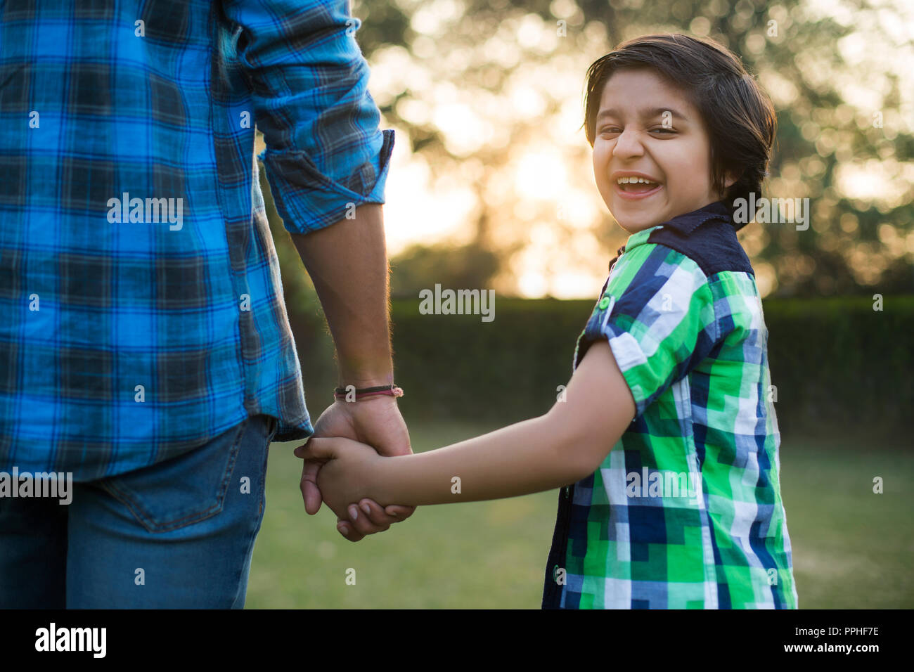 Vue arrière d'un smiling boy holding hand de son père debout dans parc. Banque D'Images