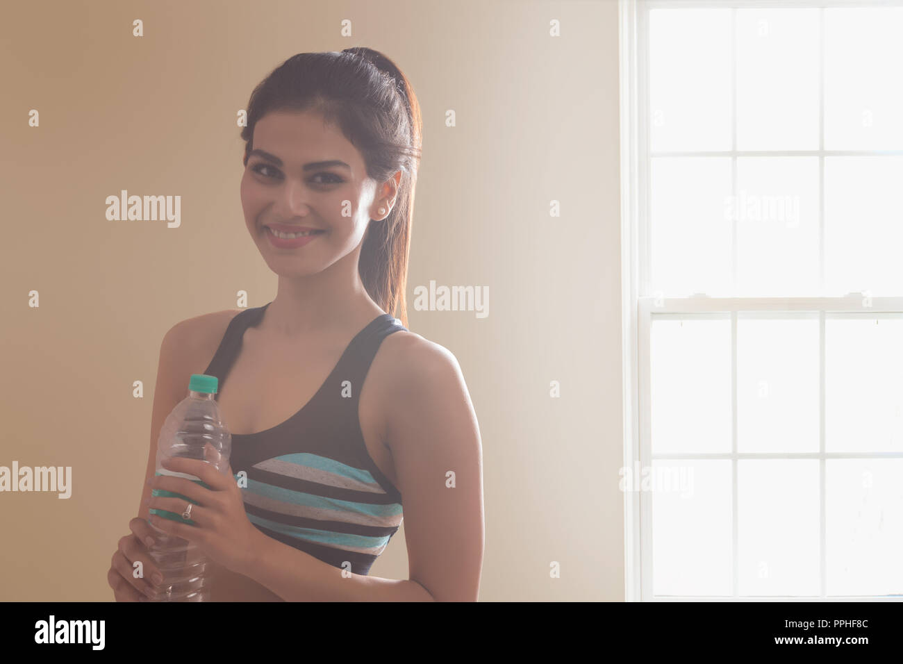 Portrait of a smiling young woman in workout clothes holding water bottle après entraînement. Banque D'Images