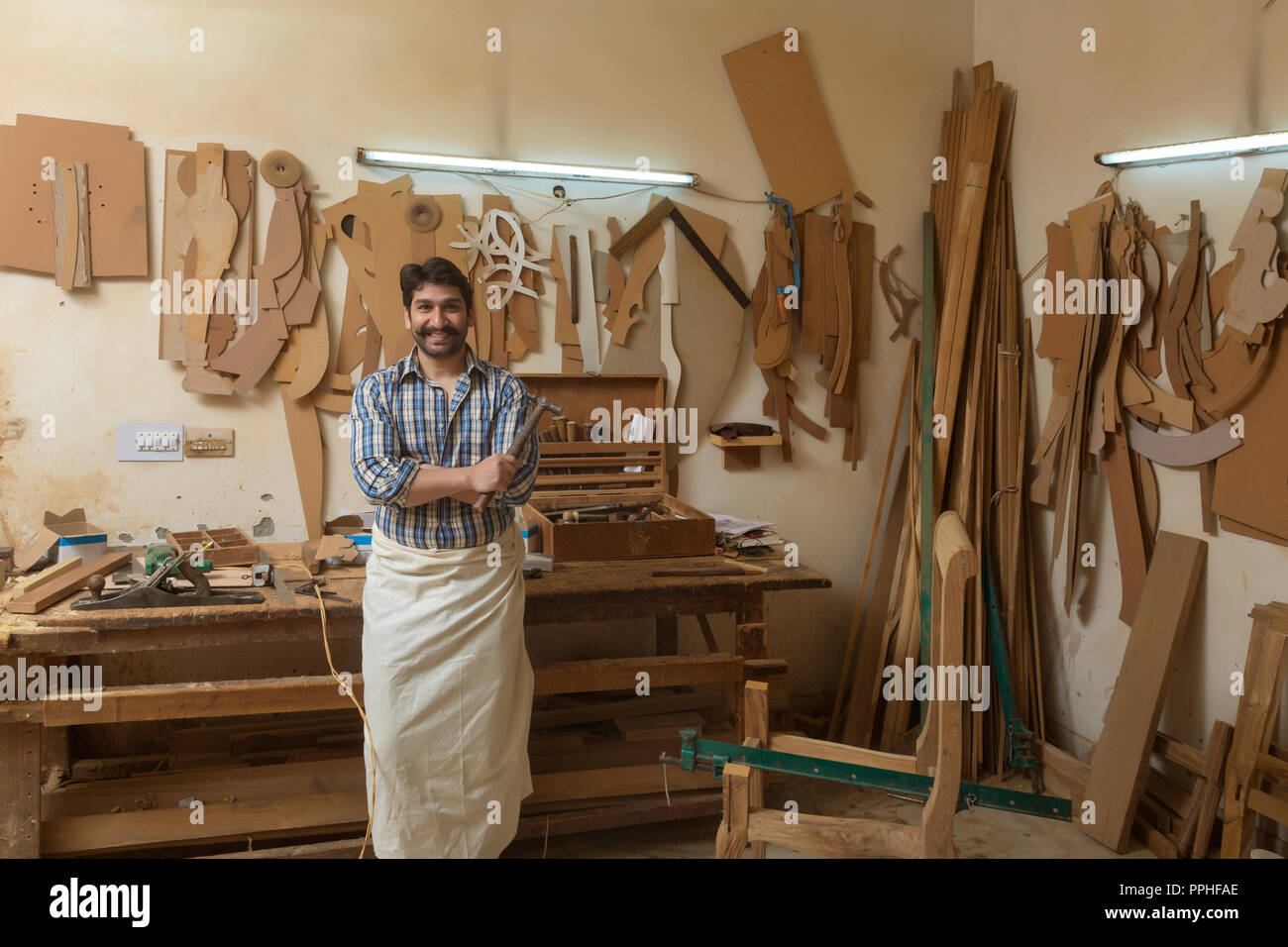 Carpenter souriant debout dans son atelier tenant un marteau avec les bras croisés. Banque D'Images
