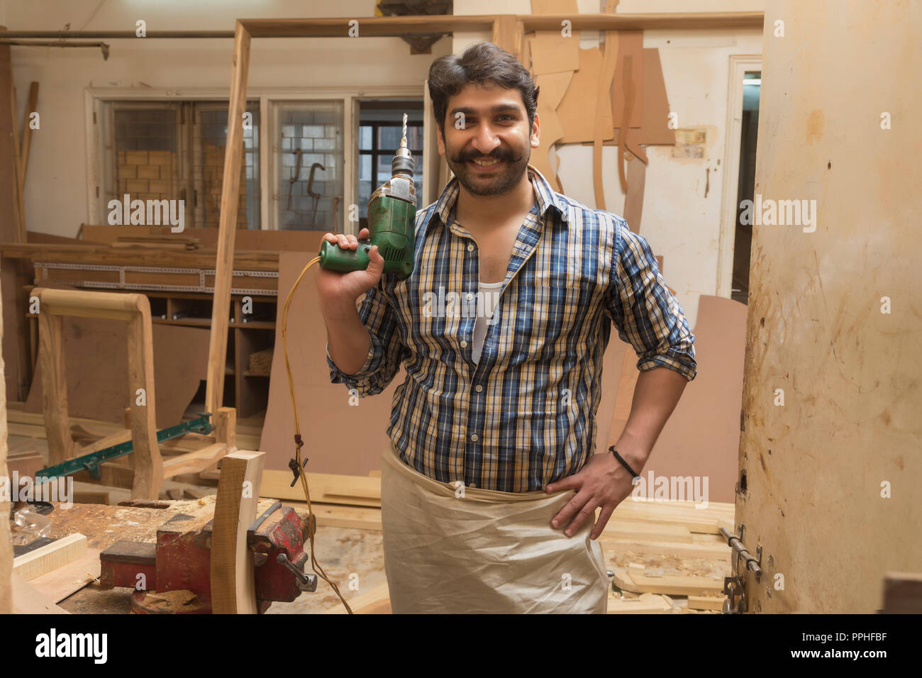 Smiling carpenter posant avec une foreuse debout dans son atelier. Banque D'Images