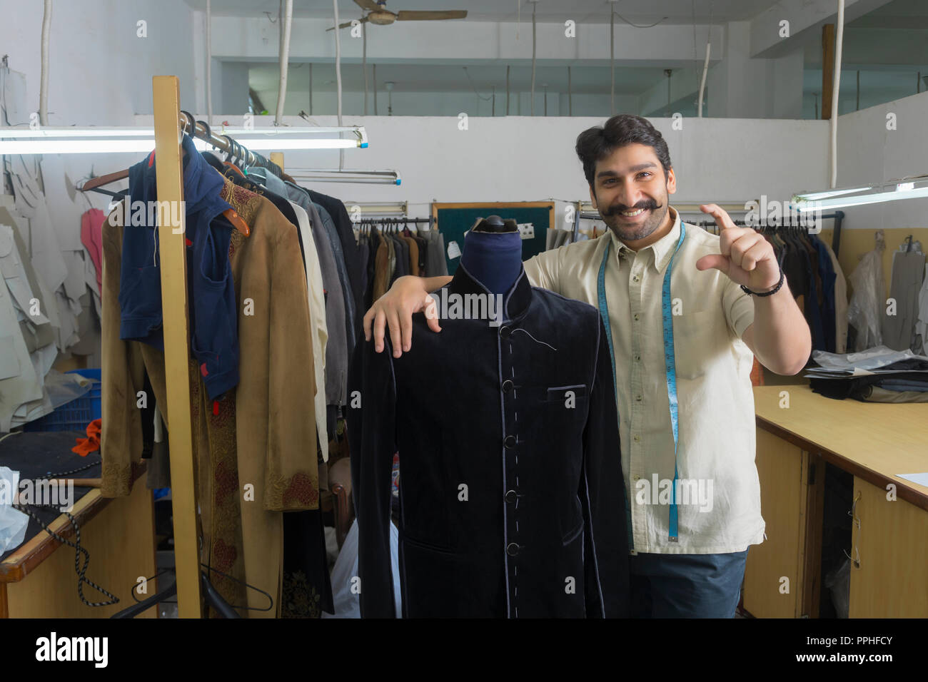 Adapter debout à côté d'un mannequin portant un manteau semi-cousues dans son atelier et montrant un geste de la tenue d'un produit dans les doigts. Banque D'Images Adapter debout à côté d'un mannequin portant un manteau semi-cousues dans son atelier et montrant un geste de la tenue d'un produit dans les doigts. Banque D'Images