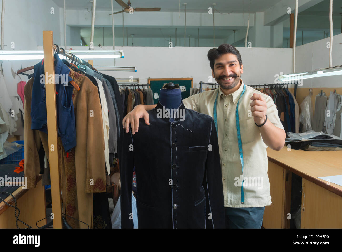Adapter debout à côté d'un mannequin portant un manteau semi-cousues dans son atelier et montrant un geste de la tenue d'un produit en main. Banque D'Images Adapter debout à côté d'un mannequin portant un manteau semi-cousues dans son atelier et montrant un geste de la tenue d'un produit en main. Banque D'Images