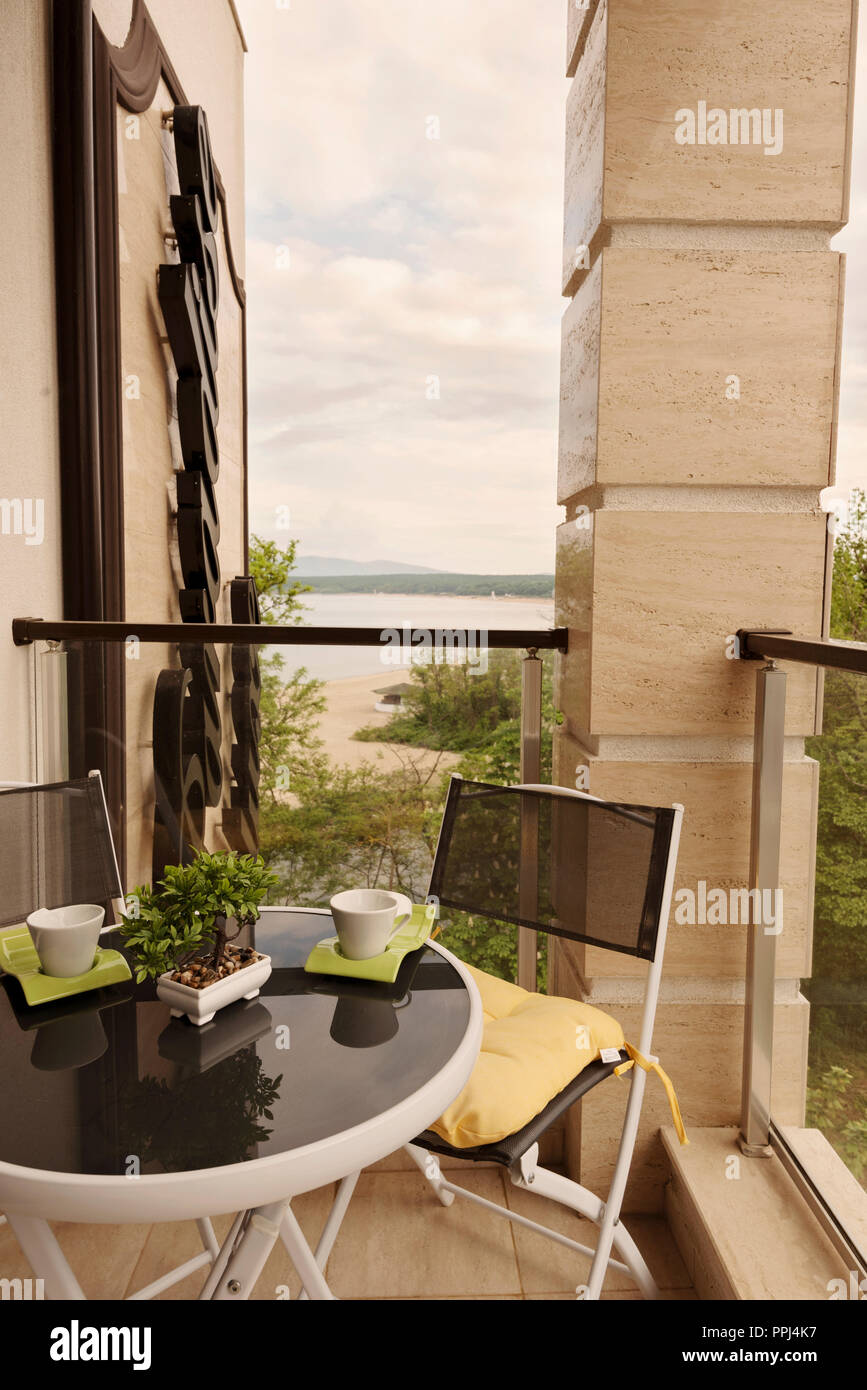 Belle terrasse ou balcon avec table avec les tasses de café et fleur sur elle et des chaises. Balcon avec vue sur la mer entouré par la nature. Chaude journée d'été Banque D'Images