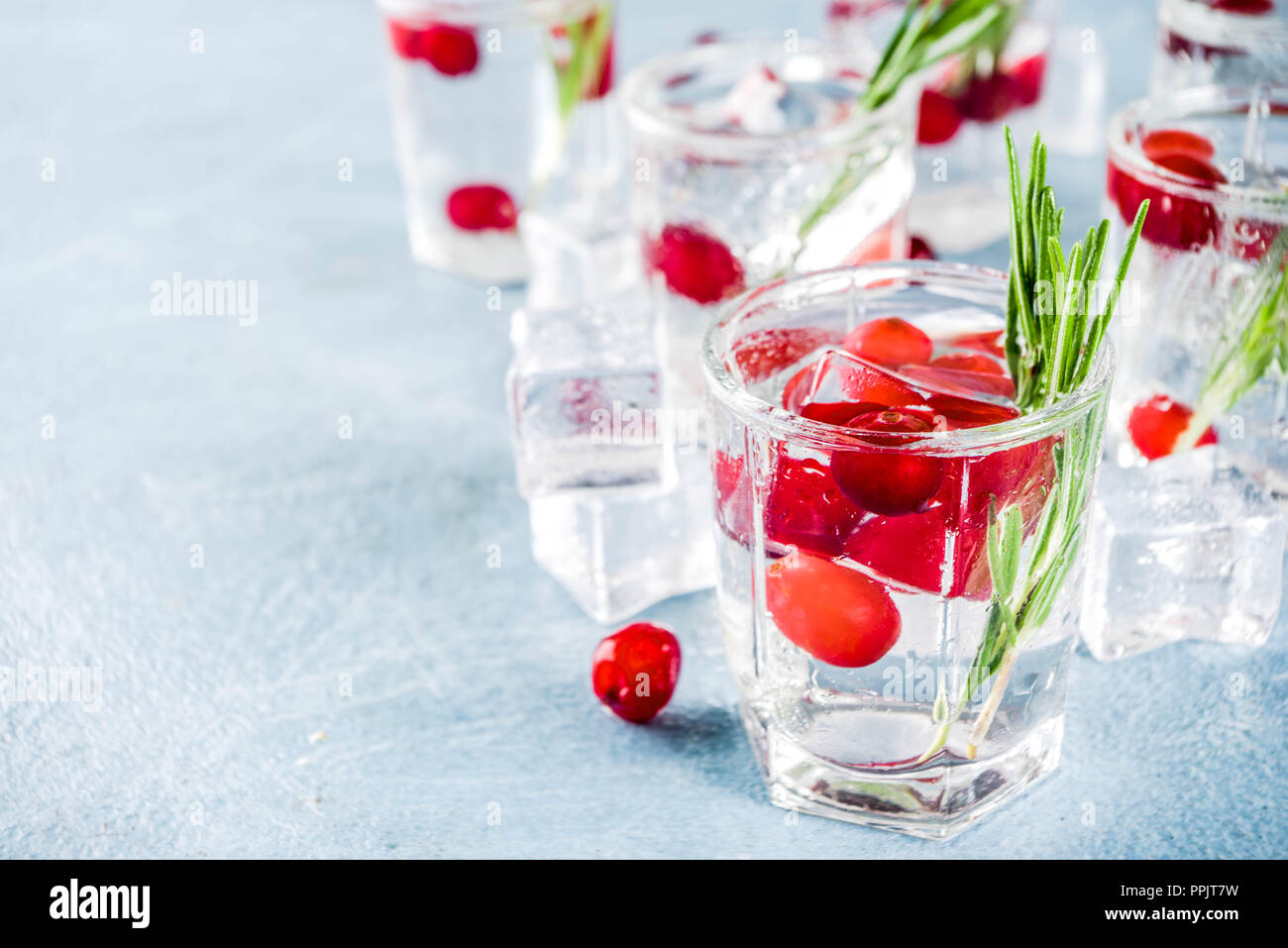 Noël ou Nouvel An cocktail de canneberges d'hiver avec le romarin, liqueurs, gin tonic, sur fond de béton bleu clair avec des cubes de glace, les baies fraîches et Banque D'Images