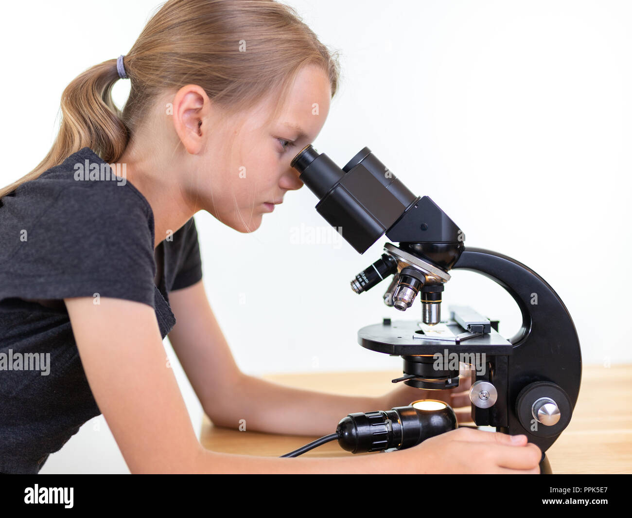 Une fille de 9 ans cherche dans un oculaire d'un microscope. Contre isolé sur fond blanc Banque D'Images