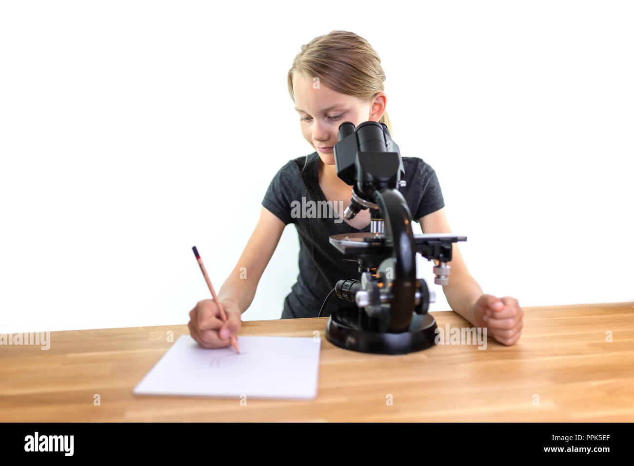 Une petite fille de 9 ans cherche dans un oculaire d'un microscope et tire ses observations sur une feuille de papier. Contre isolé sur fond blanc Banque D'Images