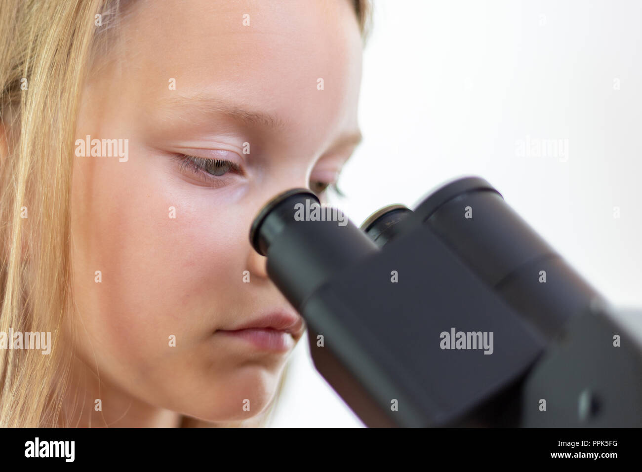 Un écolier de 9 ans blonde regarde dans l'oculaire d'un microscope. Isolé Banque D'Images