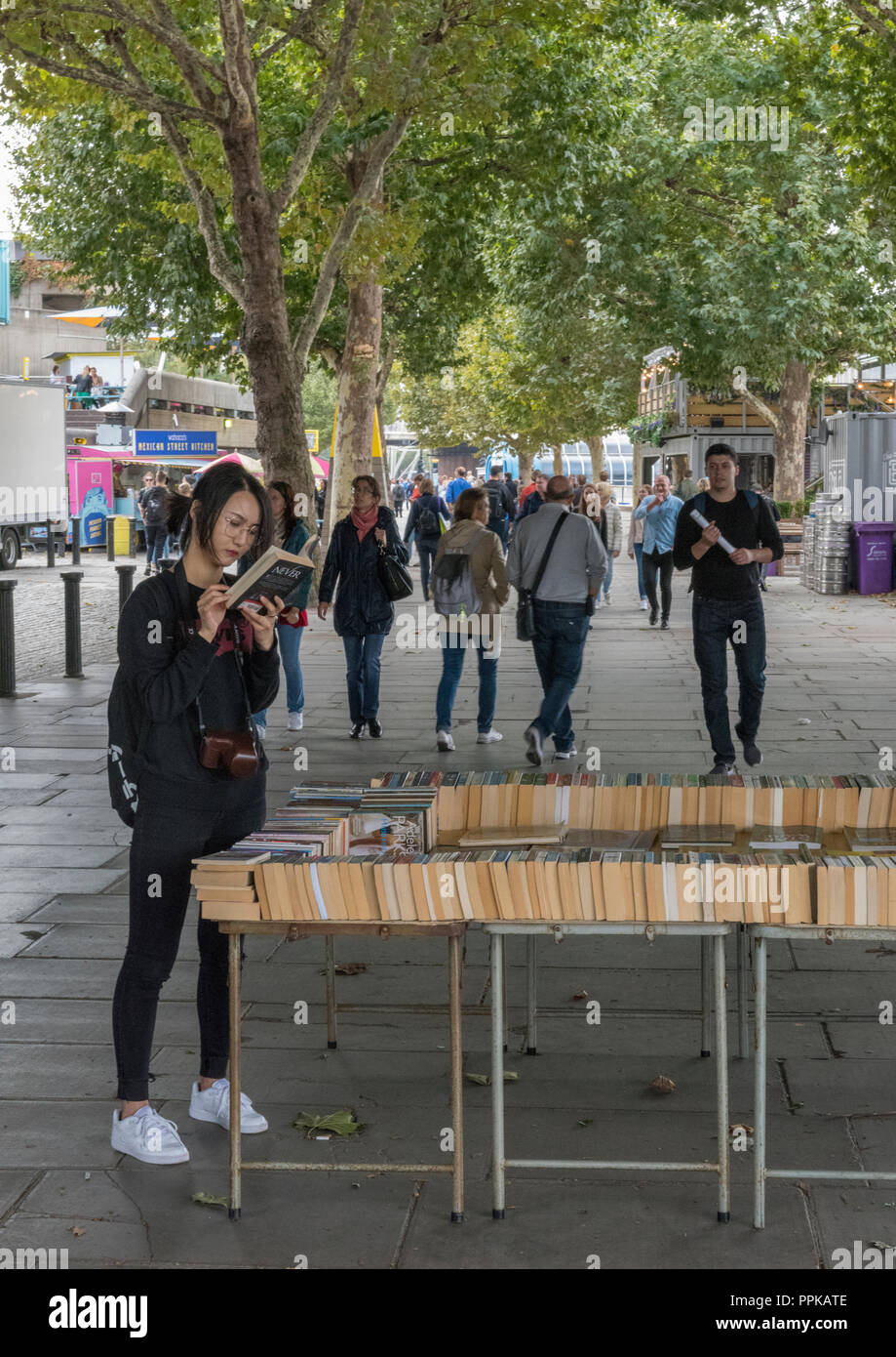 Une jeune chinoise ou japonaise ou chinoise étudiante à la recherche de livres sur la rive sud de la Tamise dans le centre de Londres, Royal Festival Hall. Banque D'Images