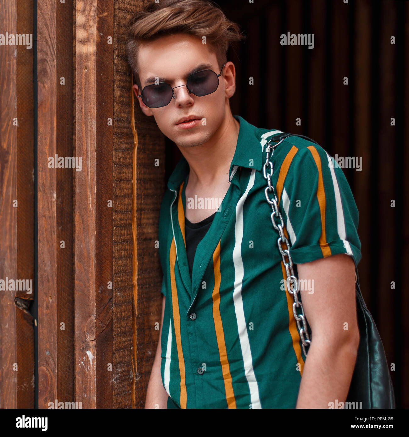 Beau mannequin homme avec des lunettes de soleil dans une chemise à rayures  de couleur se tient près d'un mur en bois Photo Stock - Alamy
