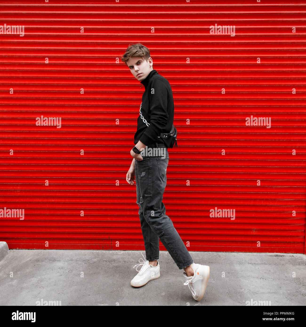 Beau modèle en vogue vogue homme en noir vêtement élégant avec blanc  sneakers posant près de red metal gate Photo Stock - Alamy
