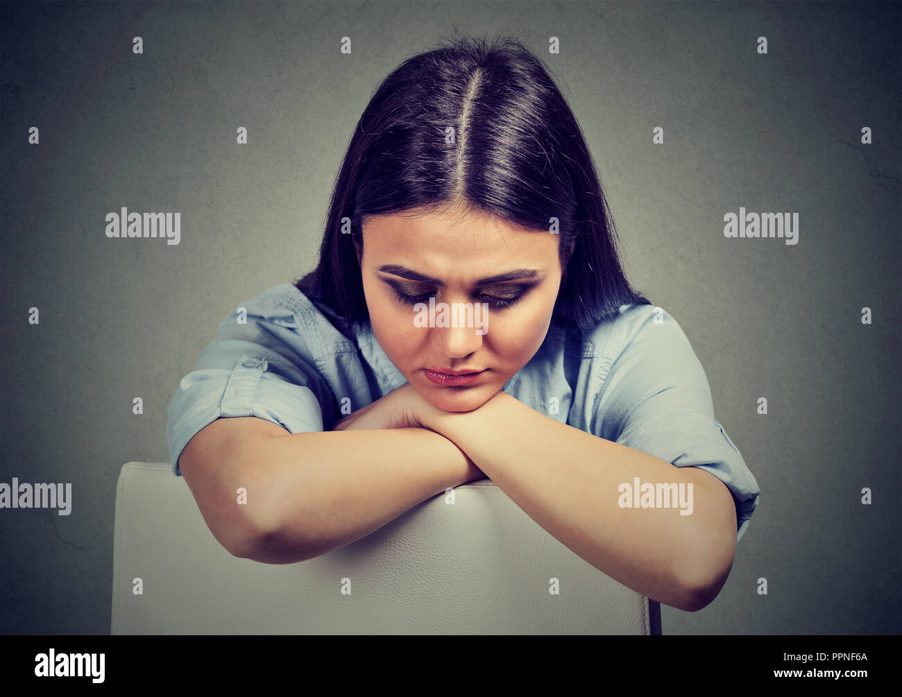 Jeune brunette woman in blue shirt s'appuyant sur une chaise dans la dépression à la colère sur fond gris Banque D'Images
