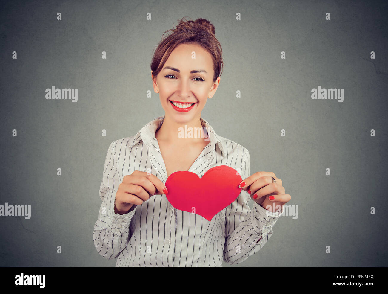 Pretty woman in shirt holding big cœur rouge sur la poitrine pleine de grands sentiments sur fond gris Banque D'Images