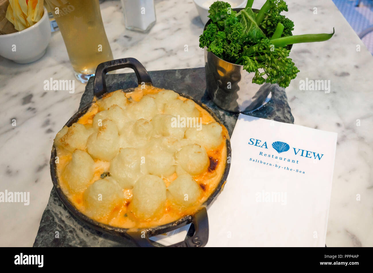 Gâteau de poisson garni de purée et parmesan servi avec les verts et une demi-pinte de lager station repas au Seaview Café Nice Nord Yorkshire UK Banque D'Images