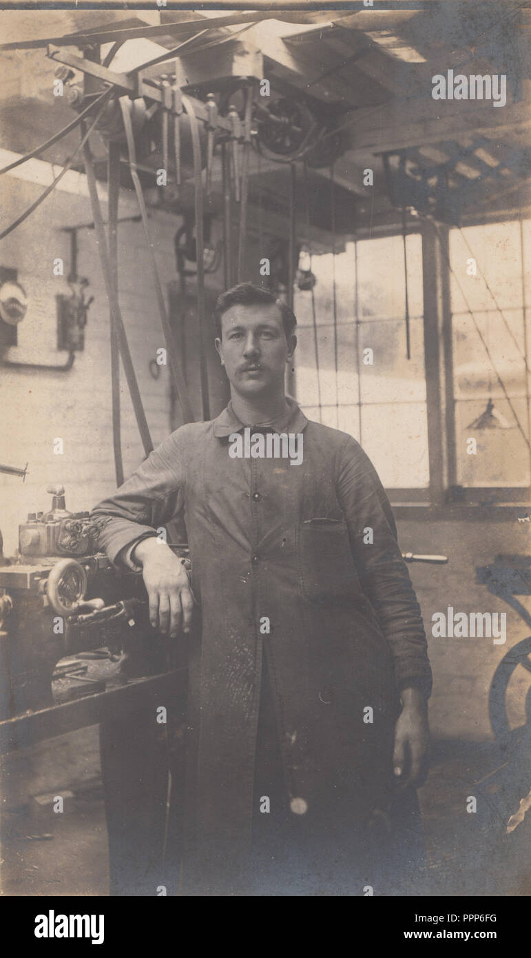 Vintage Carte postale photographique d'un homme portant une combinaison se tenait dans son atelier Banque D'Images