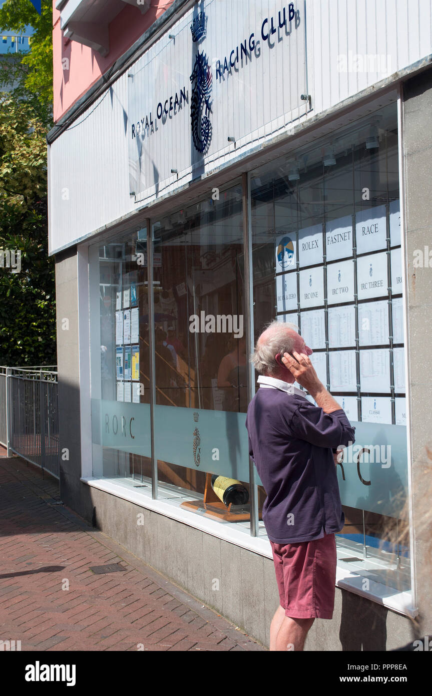 Man with mobile phone à la course à l'annexes dans la fenêtre de Royal Ocean Racing Club, High Street, Cowes, Cowes Week 2013, île de Wight, Royaume-Uni Banque D'Images