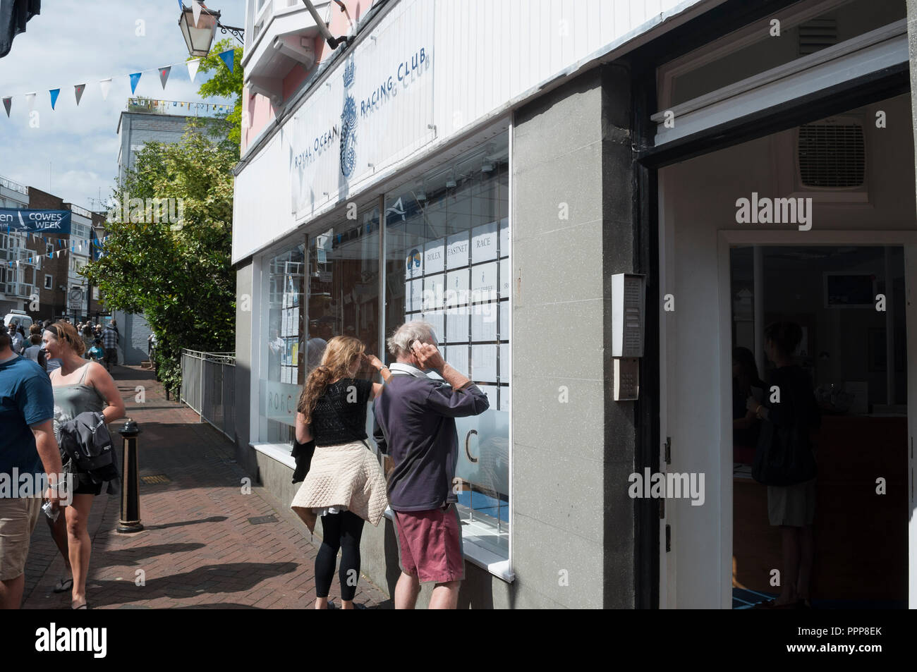 La femme et l'homme à la course de programmes affichés dans la fenêtre Royal Ocean Racing Club, High Street, Cowes, Cowes Week 2013, île de Wight, Royaume-Uni Banque D'Images