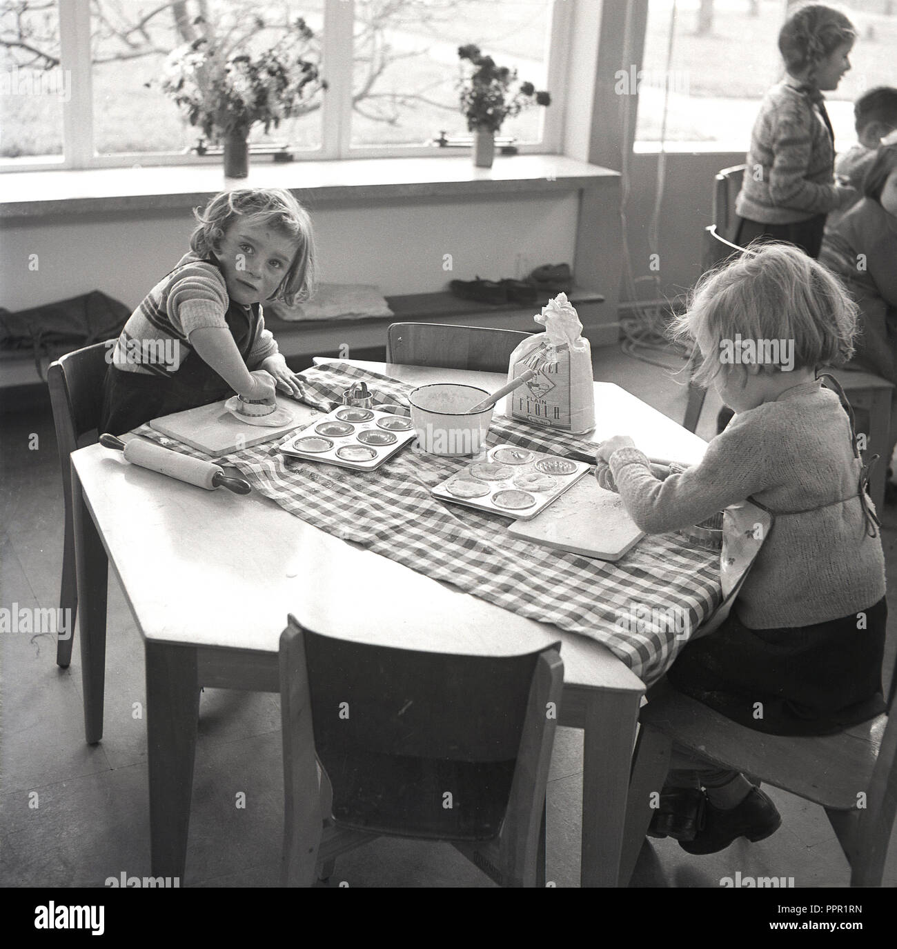 Années 1960, historiques, une école de cuisine, deux jeunes écolières assis à une table hexagonale avec un sac de farine et un bol d'eau ou de la pâte feuilletée, England, UK. Banque D'Images