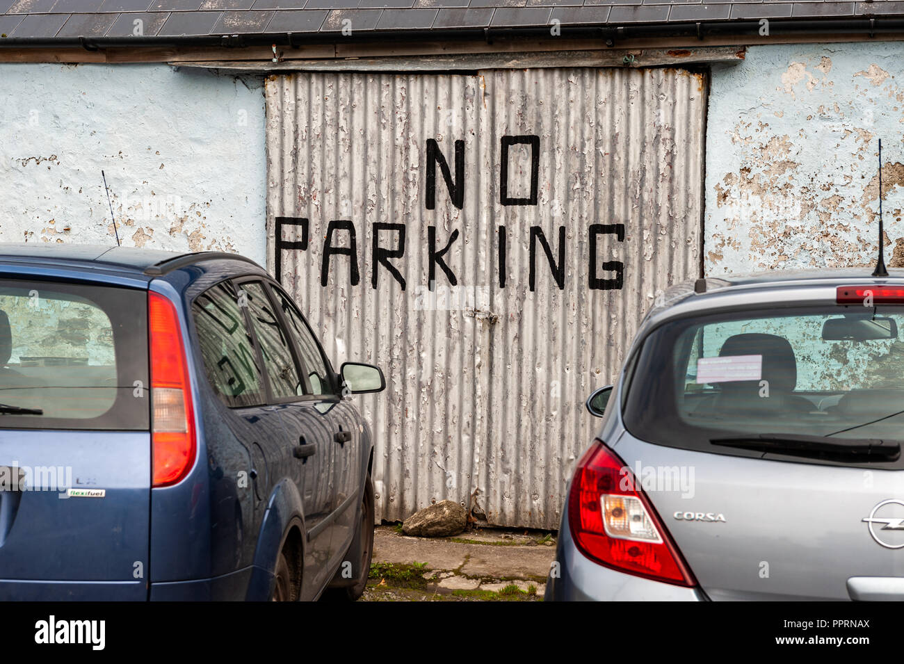 Voitures garées en face d'un No Parking sign peint sur une porte de garage à Schull, West Cork, Irlande. Banque D'Images
