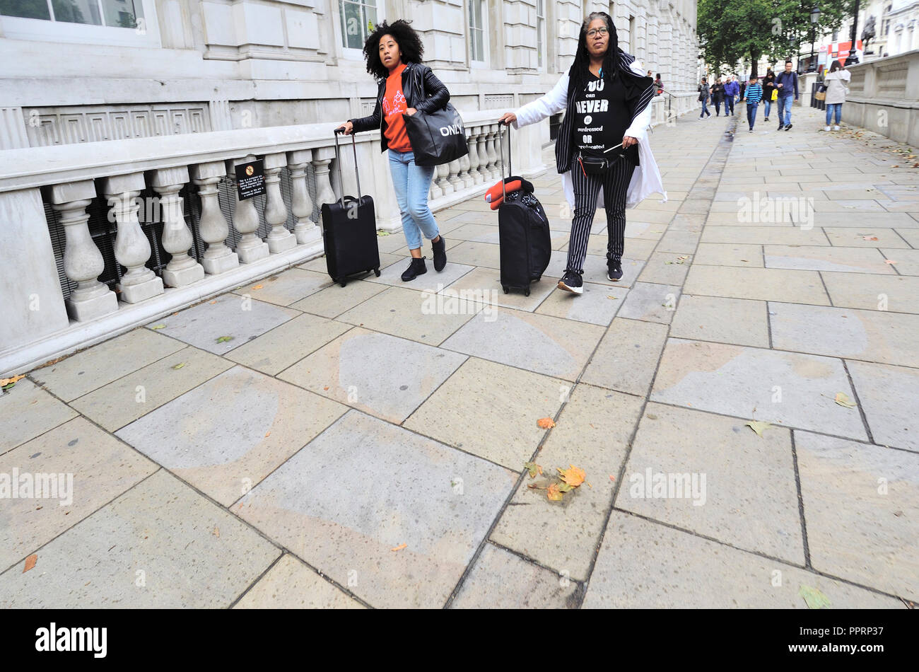 Deux femmes noires wheeling assurance à Whitehall, Westminster, Londres, Angleterre, Royaume-Uni. Banque D'Images