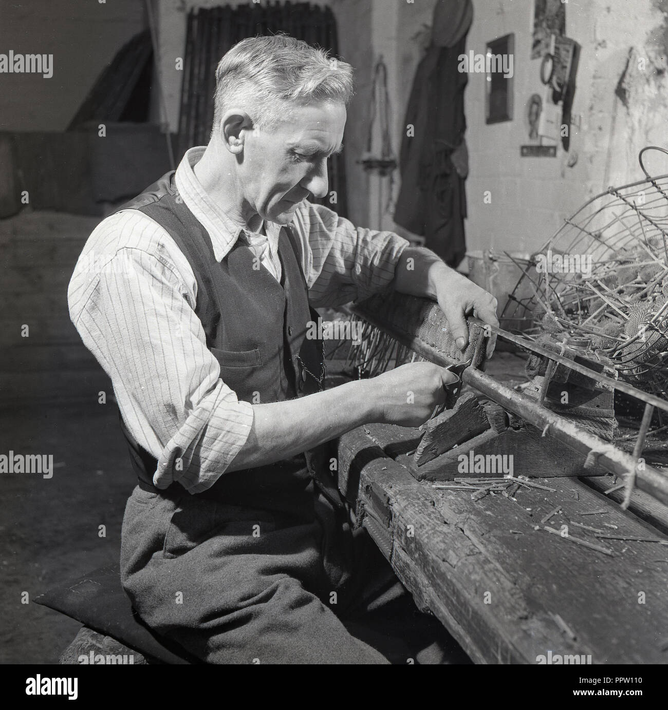 Années 1950, historiques, homme artisan à l'intérieur d'une dépendance dans une ferme de travail assis en bois à faire une certaine forme d'établi grande brosse, England, UK. Banque D'Images