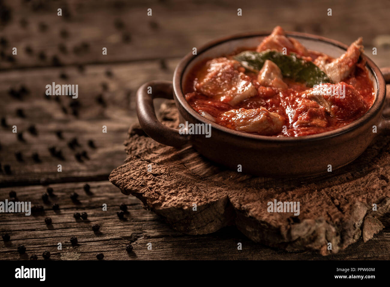 De délicieux plats de viande et de tomates repas servi dans un plat de cuisson en céramique avec petites poignées sur fond de table en bois Banque D'Images