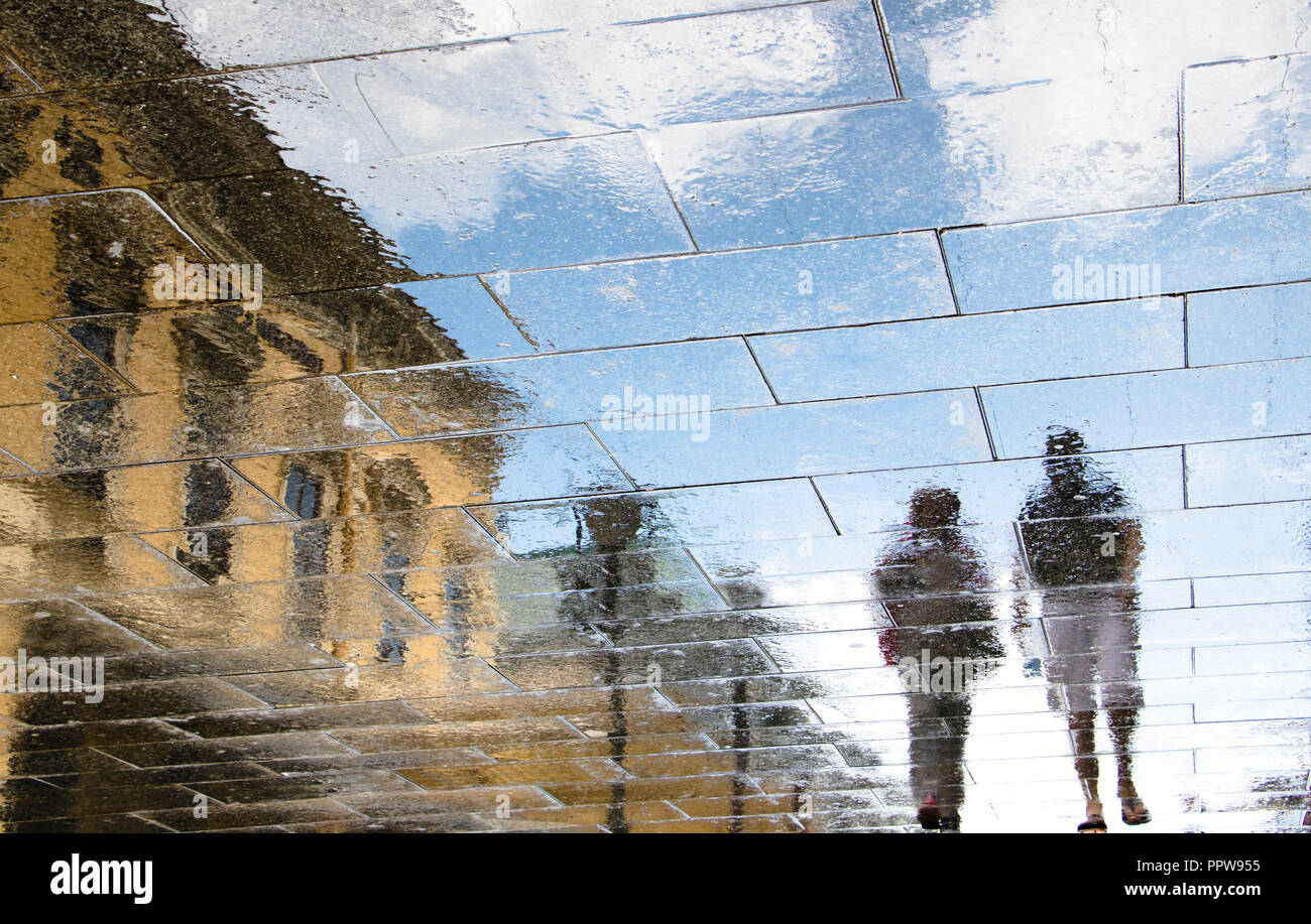 Réflexion floue ombre silhouette dans une flaque d'âge mûr marche sur la rue ville humide après la pluie Banque D'Images