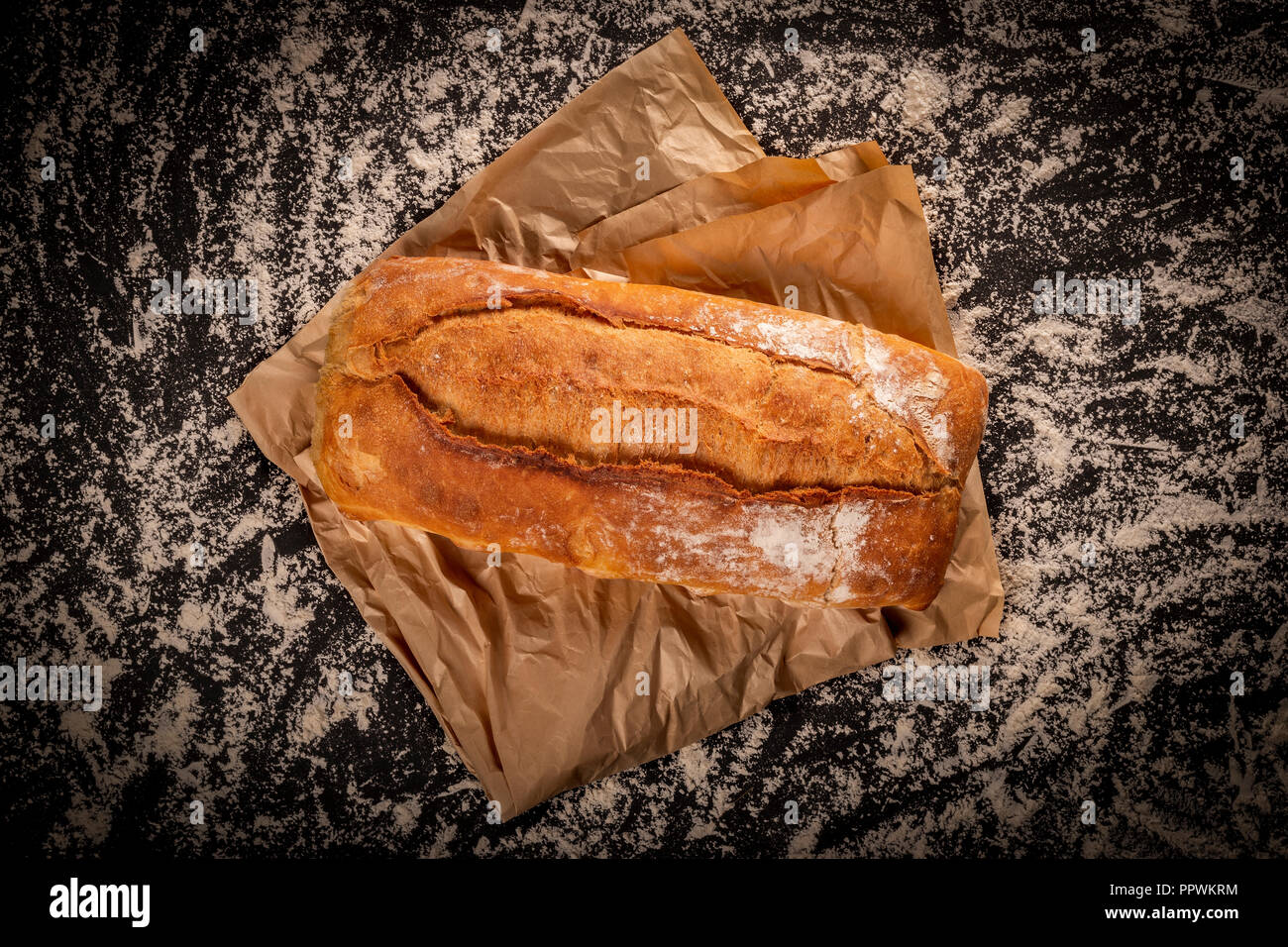 Au-dessus de la maison rustique de miche de pain sur morceau de papier sulfurisé sur le dessus de table dans la farine blanche Banque D'Images