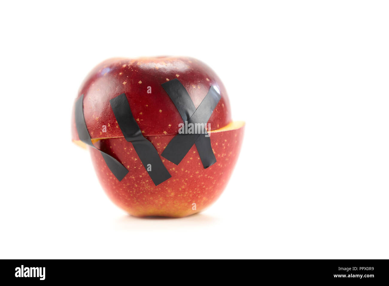 Deux moitiés d'une pomme rouge tenue ensemble par du ruban adhésif noir isolé sur fond blanc. Banque D'Images