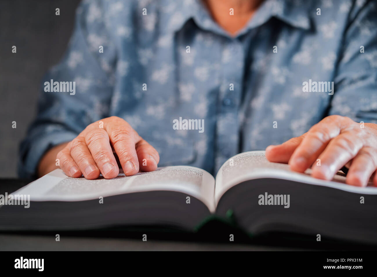 Vieille Femme à la lecture livre épais à la maison. Grand-mère avec Bible. Personne âgée retraitée concentré de rides sur les mains doigt suit attentivement la page sur le papier dans la bibliothèque Banque D'Images