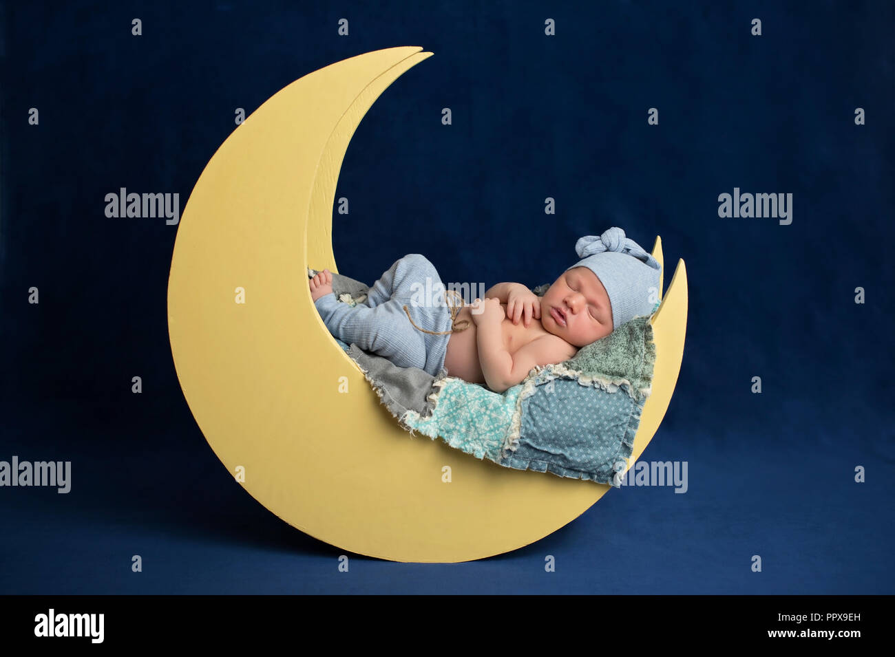 Studio portrait d'un nouveau-né âgé de dix jours en portant des bas de pyjama bébé garçon et un coin couchage. Il est en train de dormir sur une lune posing prop. Banque D'Images