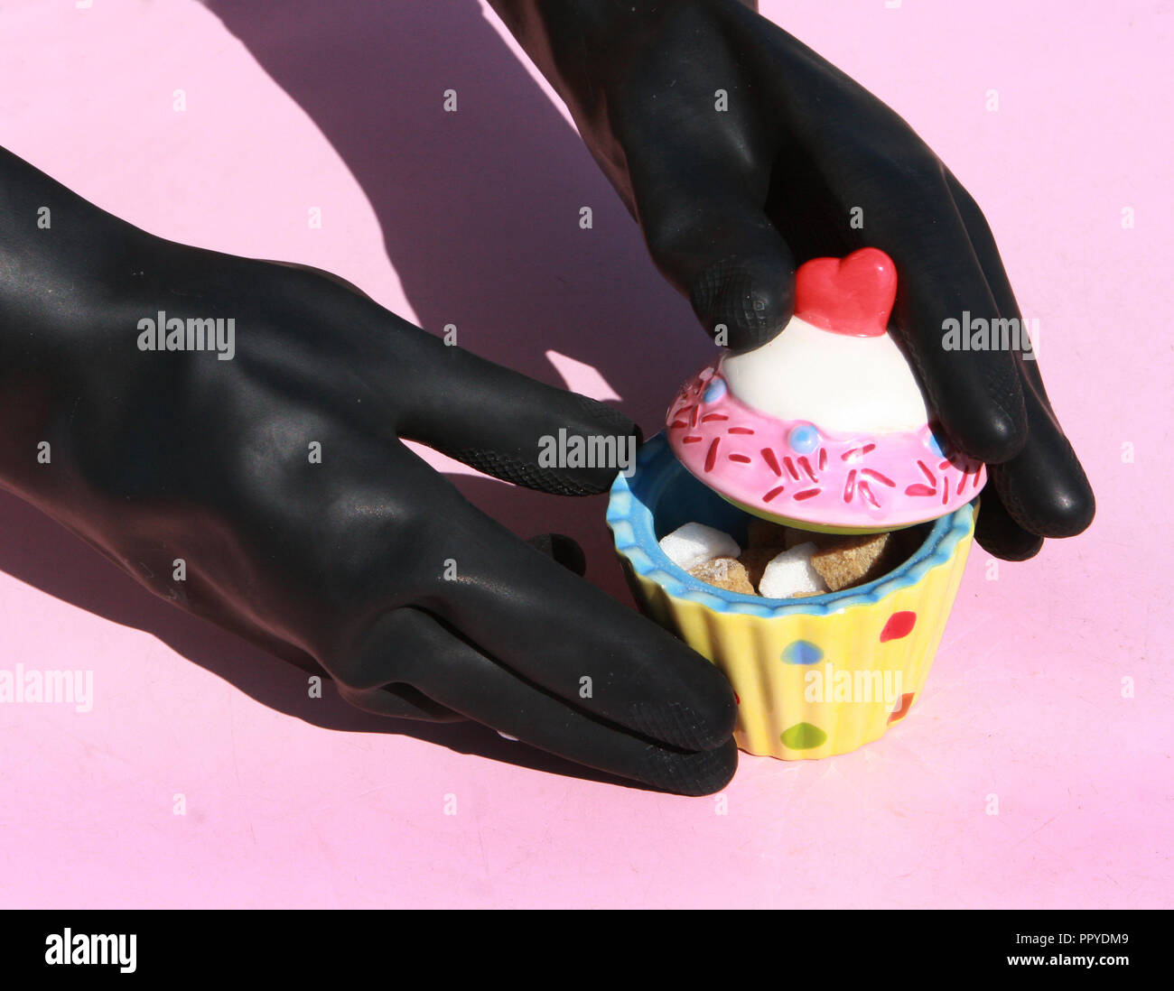 Gants en caoutchouc noir holding pot sucre cupcake Banque D'Images