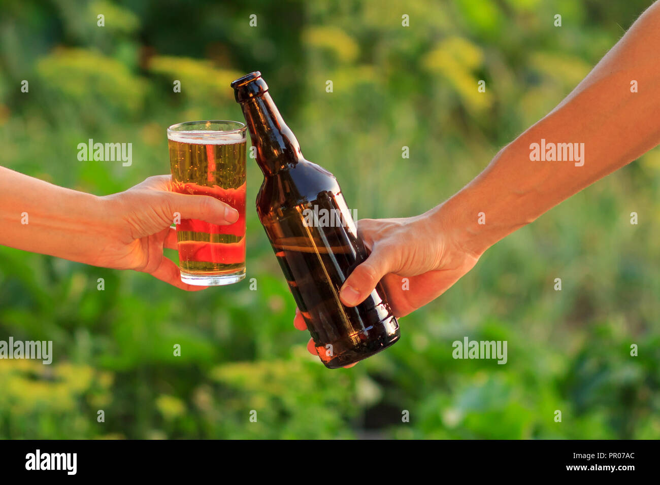 Portrait de femme et l'homme qui retentit verre de bière et une bouteille de bière ensemble en arrière-plan flou vert naturel. Femme clinked son verre contre Banque D'Images