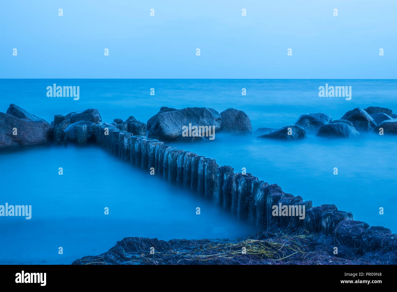 Des pierres sur la rive dans l'eau laiteuse bleuté après le coucher du soleil au cours de l'heure bleue à Rabylille Beach, à l'île de Moen, Danemark, Scandinavie, l'Europe. Banque D'Images