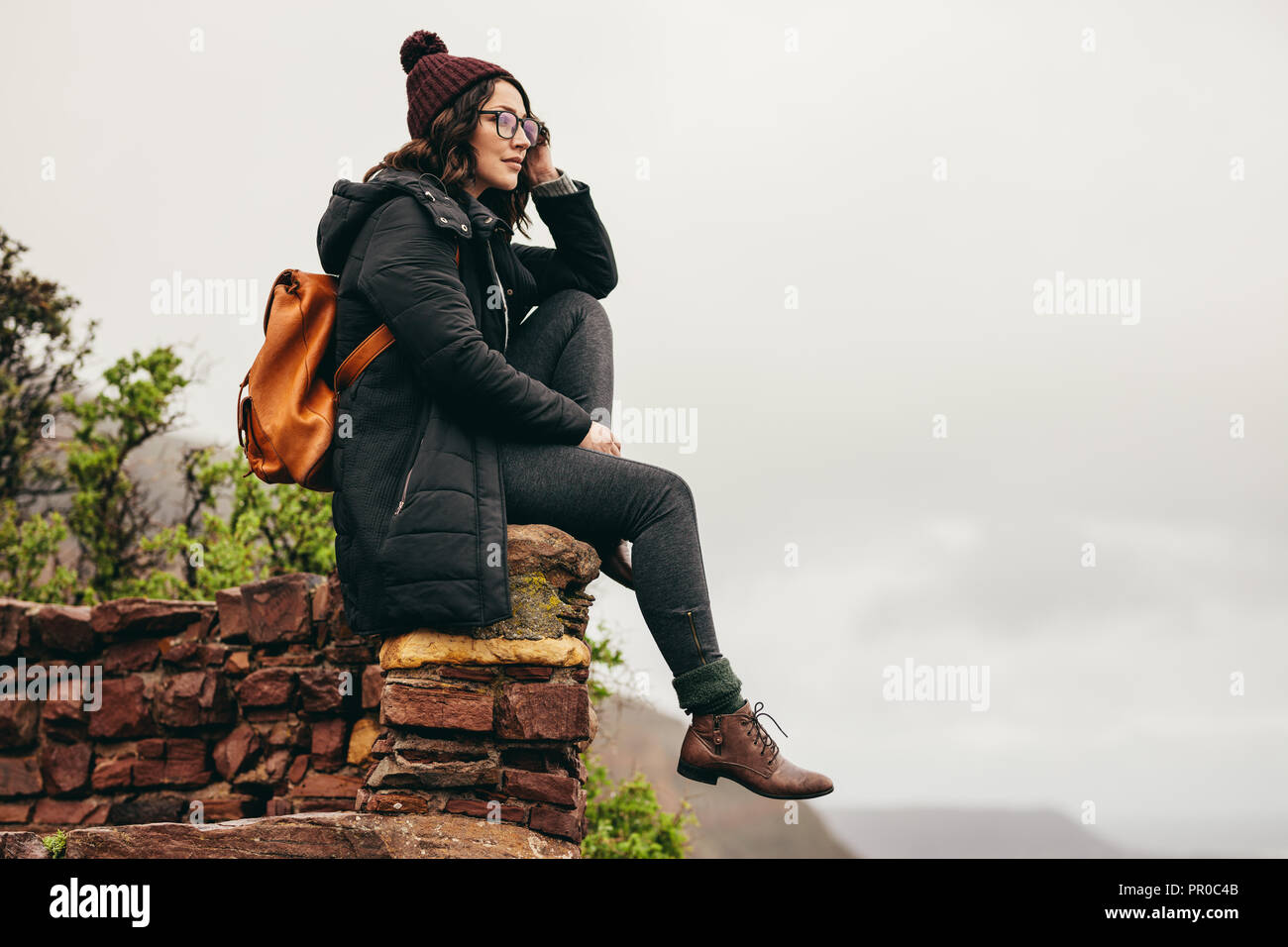 Jeune femme assise sur un mur de pierre à flanc et en contemplant la vue. Woman resting on Mountain et à la recherche à la vue. Banque D'Images