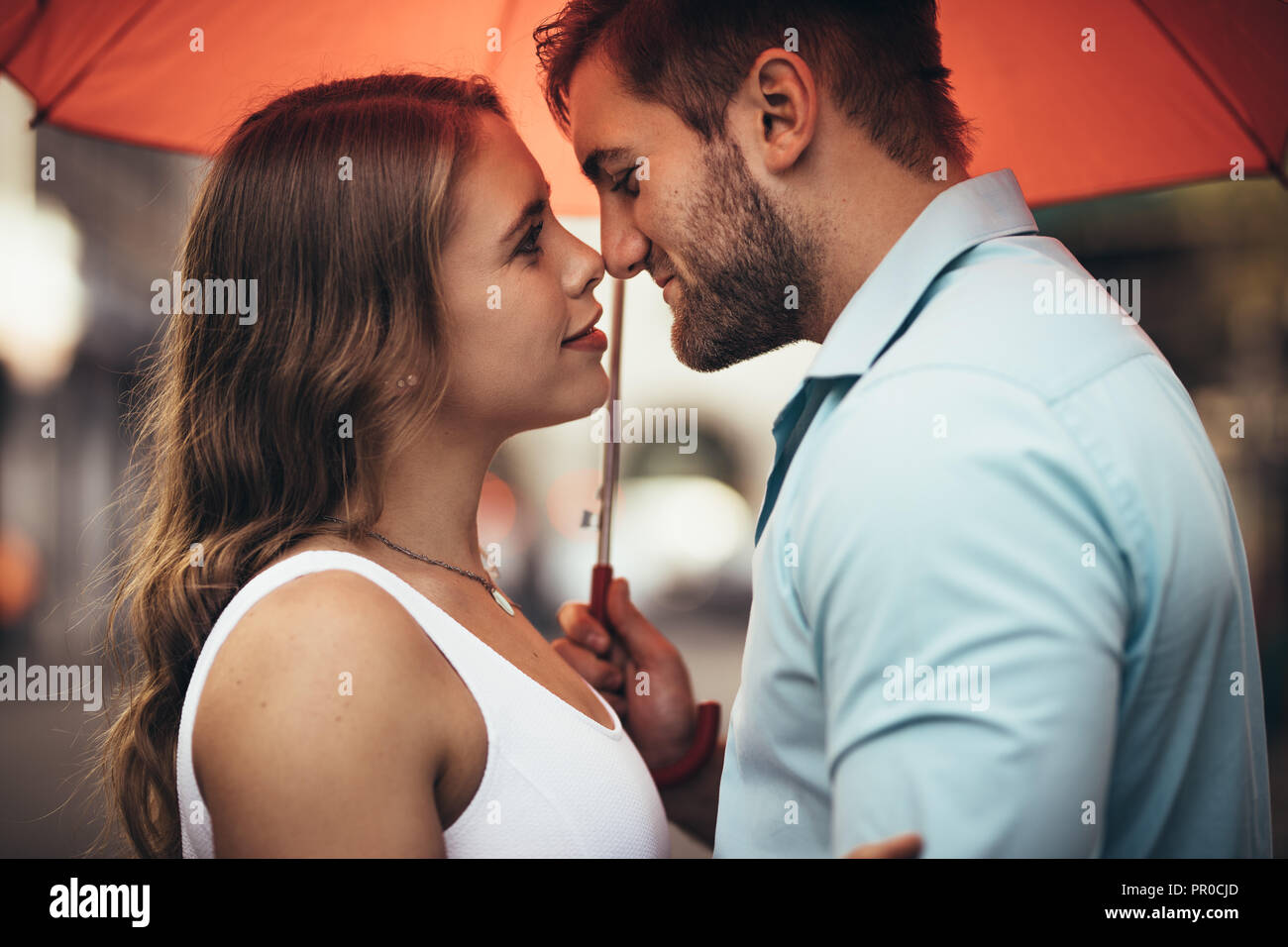 Close up of a couple standing proche sous un parapluie de toucher leurs nez. L'homme et de la femme dans l'amour se tenant ensemble holding an umbrella in rain outdoor Banque D'Images