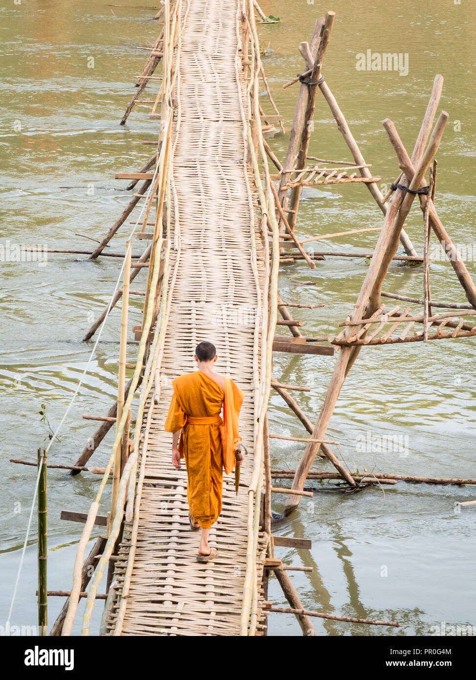 Orange-clad le moine bouddhiste traversant un pont de bambou, Luang Prabang, Laos, Indochine, Asie du Sud, Asie Banque D'Images
