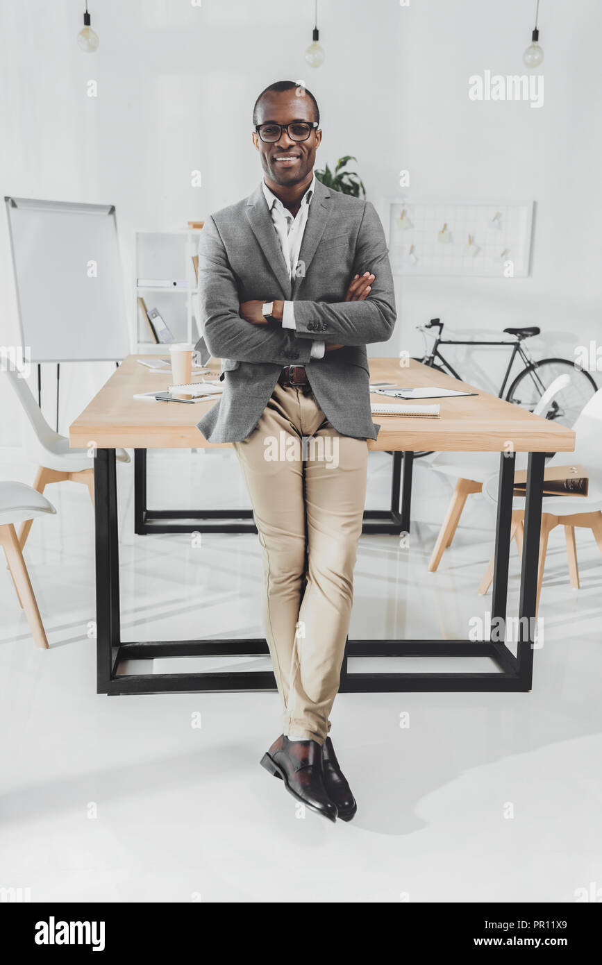Smiling african man leaning on table avec les bras croisés à l'espace de bureau Banque D'Images