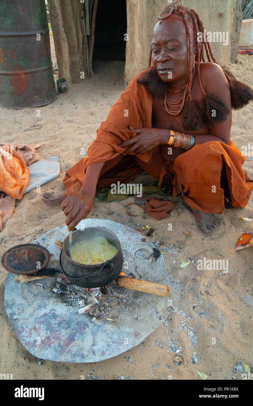 L'un rouge senior ochred femme Himba cuisiner son repas sur un feu ouvert, Village Puros, près de Sesfontein, Namibie, Afrique Banque D'Images