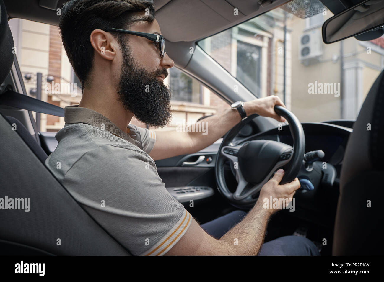 Les gens heureux et fait face à la ville de concept. Un homme barbu positive au volant de sa voiture à travers la ville tout en souriant. Profiter de chaque jour instants simples Banque D'Images