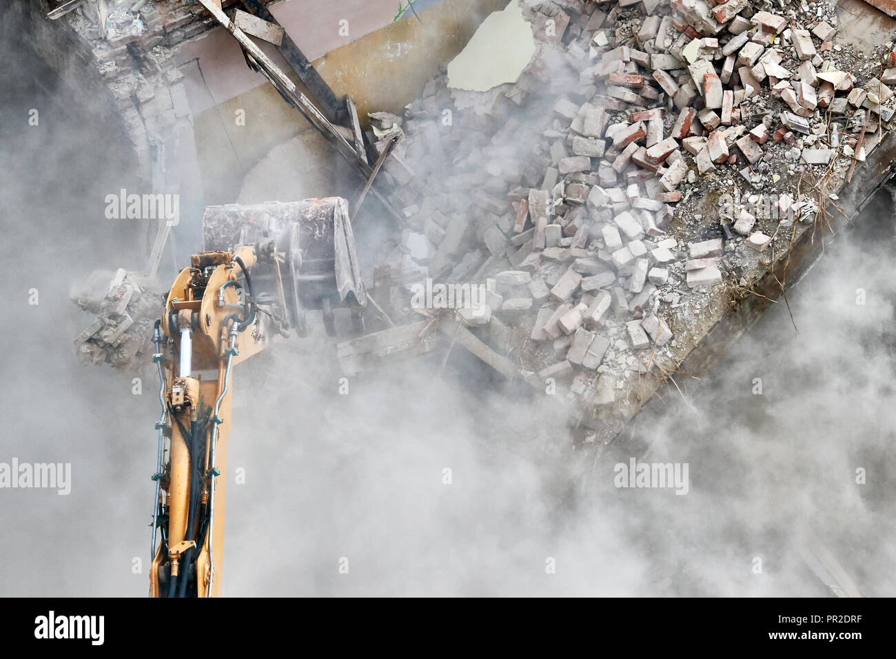Démolition de bâtiment avec une excavatrice dans un nuage de poussière. Banque D'Images
