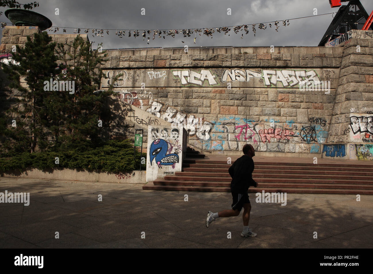 Passe devant l'athlète par la base de l'ancien monument de Staline couvert de graffitis à Letná Letenské sady (PARC) à Prague, République tchèque. Vieilles bottes se bloque sur le câble électrique à l'arrière-plan. Selon la légende locale, les adolescents chaussures jeter sur le câble, lorsqu'ils perdent leur virginité. Banque D'Images