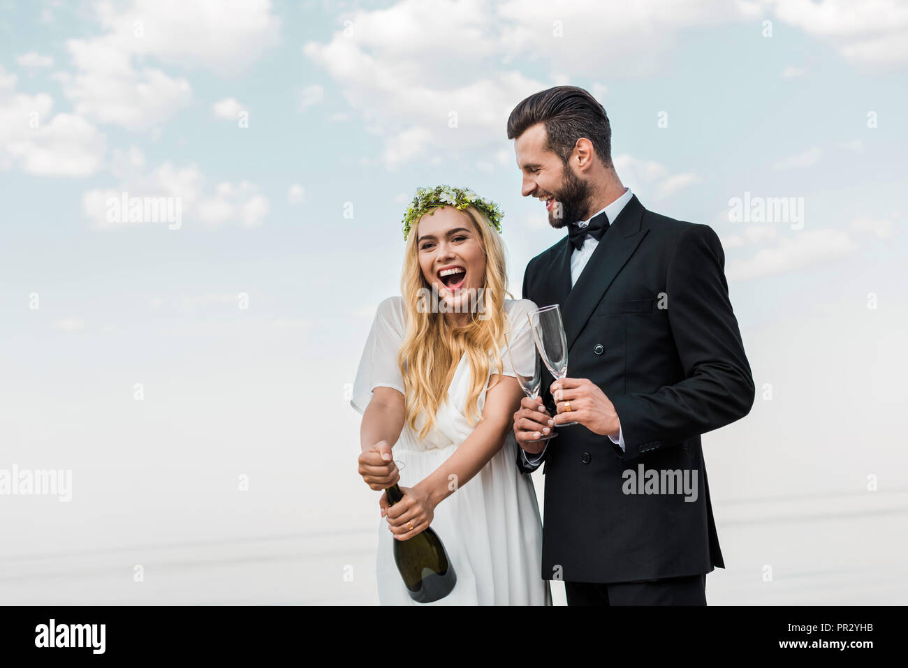 Happy bride en robe blanche bouteille de champagne sur la plage d'ouverture Banque D'Images