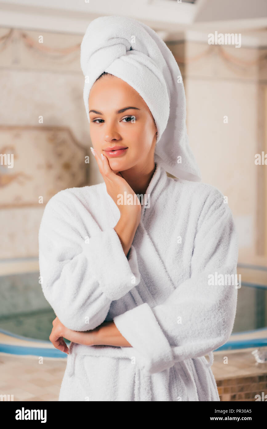 Smiling woman in white terry peignoir avec une serviette sur la tête dans le centre de spa avec piscine Banque D'Images