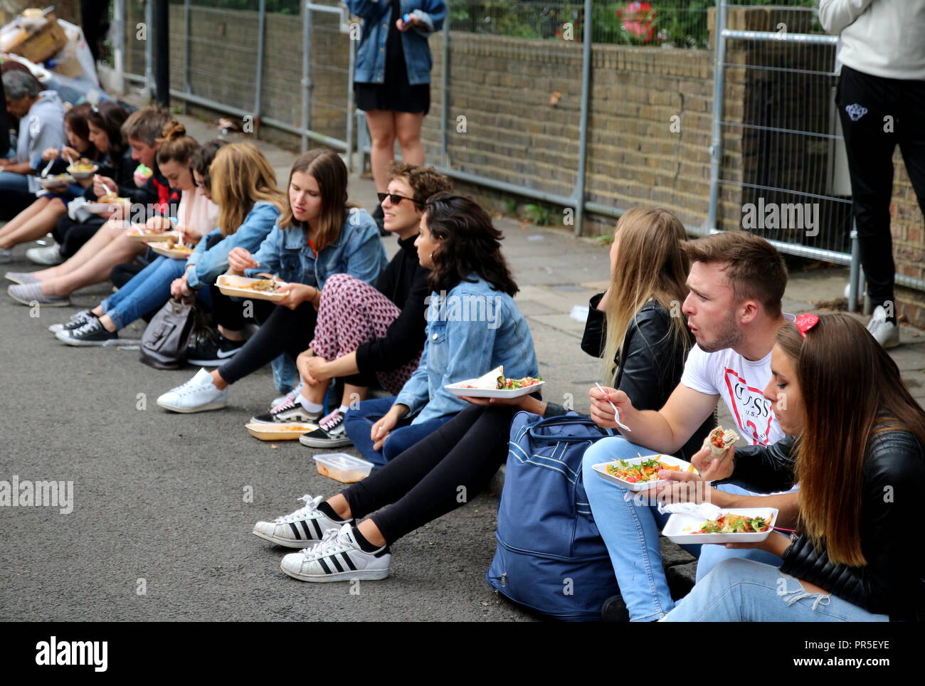 Londres, Royaume-Uni - 27 août 2018 carnaval de Notting Hill : Groupe d'adolescents manger de délicieux aliments rapide assis dans la rue Banque D'Images