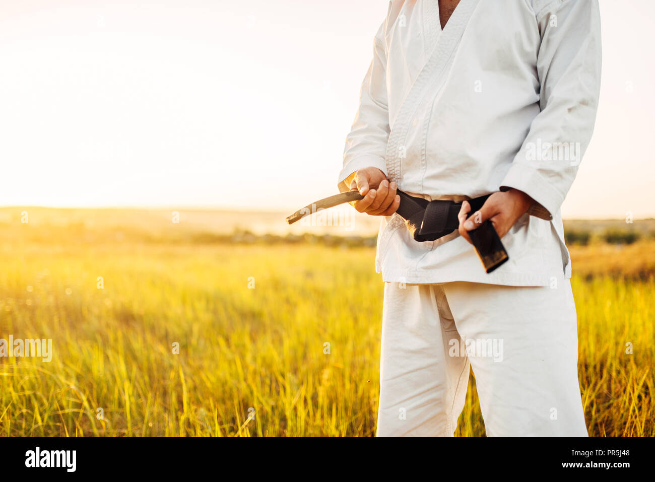 Karaté mâle fighter en kimono blanc avec ceinture noire, d'été à l'extérieur sur l'arrière-plan. Formation d'art martiaux piscine Banque D'Images