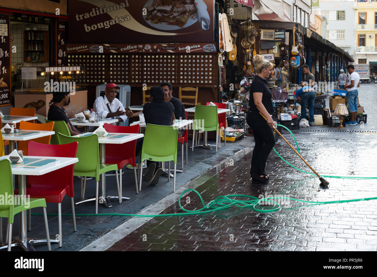 Dimanche après-midi, un employé de snack-bars ouverts à recevoir ses clients, est le nettoyage de la rue en face de la barre, Athènes Grèce Banque D'Images