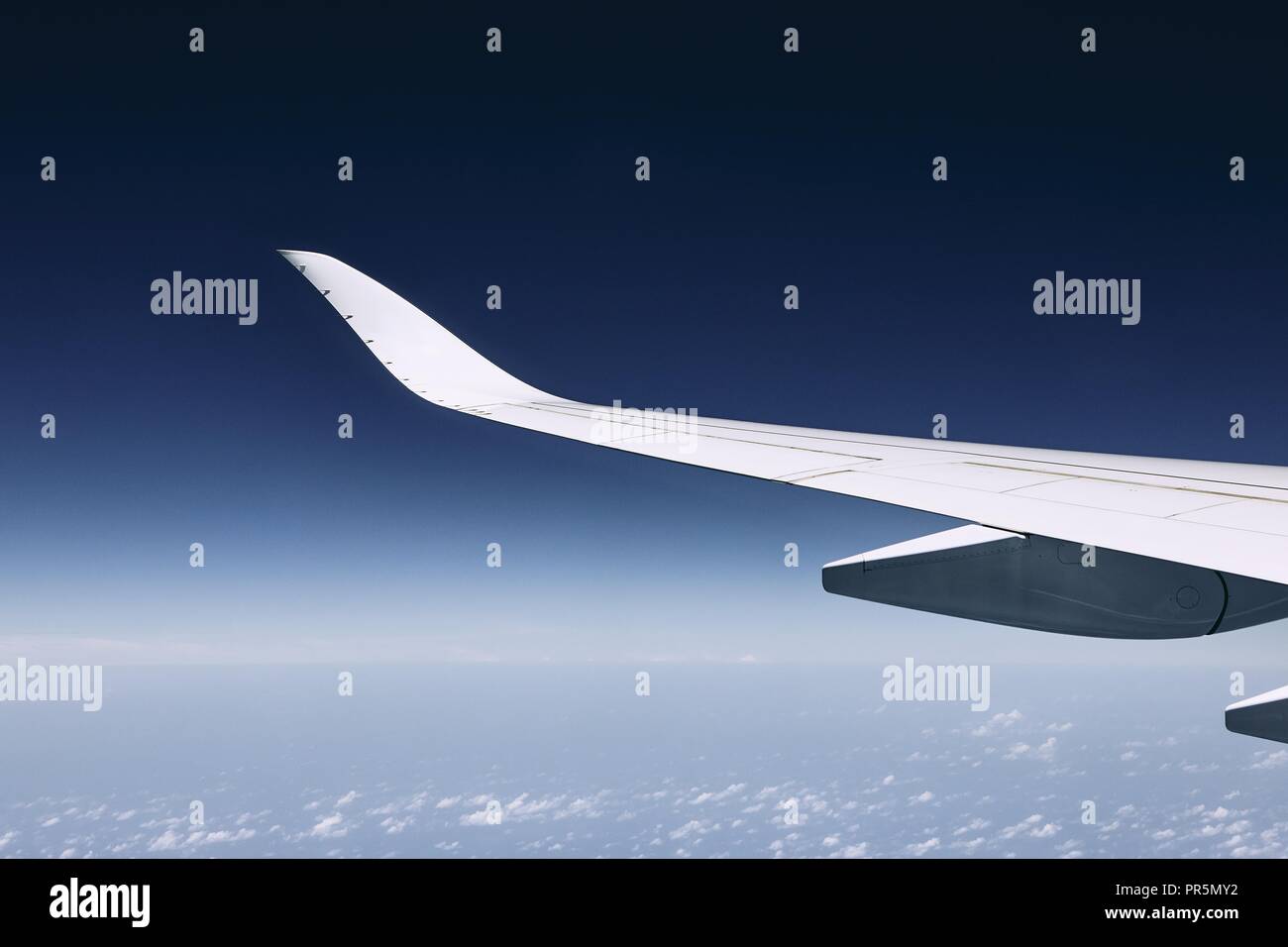 Aile de vol d'un avion moderne plus de nuages contre ciel bleu foncé. Banque D'Images