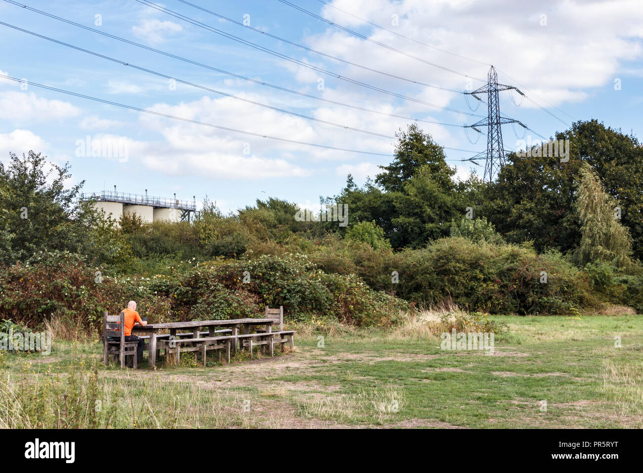Homme assis à un Banc et table de pique-nique public dans un pré sur les marais de Walthamstow, London, UK Banque D'Images