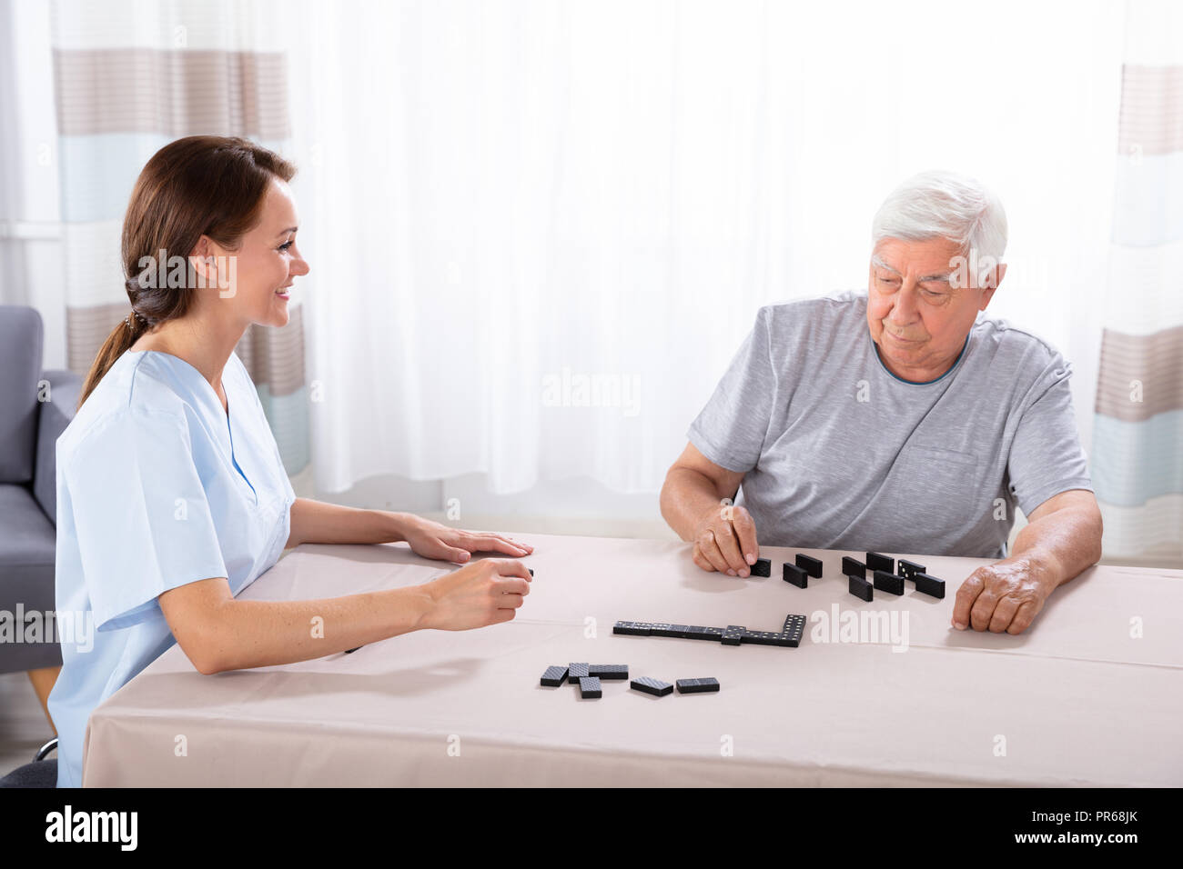 Jeune femme à la conciergerie à vieil homme jouant aux dominos sur 24 Banque D'Images
