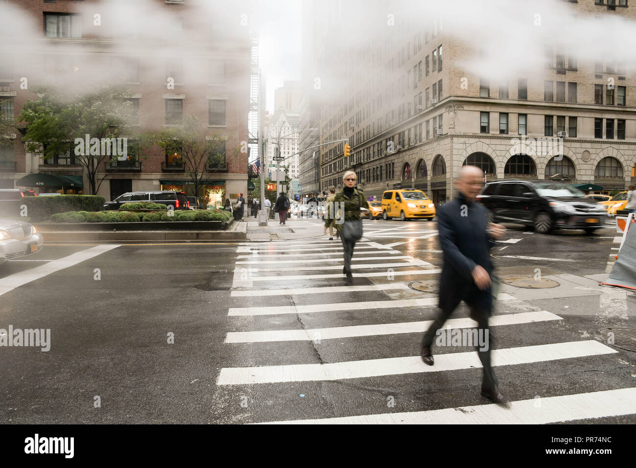 Les piétons utiliser un passage pour piétons à l'intersection de l'avenue Park et East 57th Street sur une matinée pluvieuse dans la ville de New York. Banque D'Images